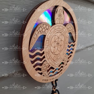 K&ouml;nnte beinhalten: Ein Holzausschnitt einer Schildkr&ouml;te mit einem Mandala-Design in der Mitte. Die Schildkr&ouml;te ist von Wellen umgeben und die Worte "Made in Kelowna BC" sind unten sichtbar. Die Schildkr&ouml;te ist in Braunt&ouml;nen bemalt und das Mandala in Blaut&ouml;nen und Gr&uuml;nt&ouml;nen.