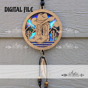 May include: Wooden circular ornament featuring a cowboy hat and boots design with a holographic background. The ornament includes the text "DIGITAL FILE" and "MADE IN KELOWNA BC, CAN". A feather and beads hang from the bottom.