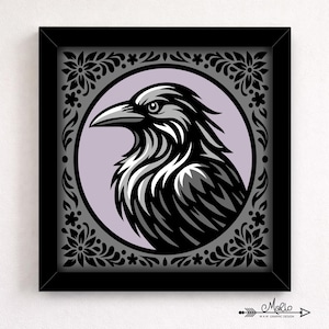 Puede incluir: Impresión artística enmarcada con una ilustración estilizada de un cuervo. El cuervo está representado en negro, blanco y gris, sobre un círculo lavanda. El marco negro tiene un diseño de borde floral. La firma del artista está en la esquina inferior derecha.