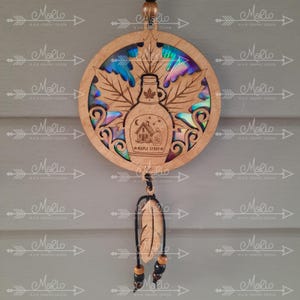 May include: A wooden maple syrup bottle charm with a holographic maple leaf design. The charm is hanging from a black cord with a wooden feather and beads.