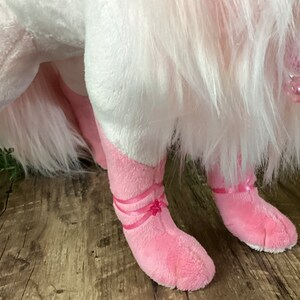May include: Pink plush toy with white fur, wearing pink ballerina shoes with pink ribbons. The toy has a pink nose and a pink tail.
