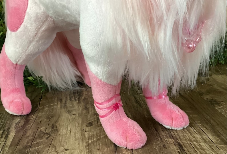 May include: Pink plush toy with white fur, wearing pink ballerina shoes with pink ribbons. The toy has a pink nose and a pink tail.