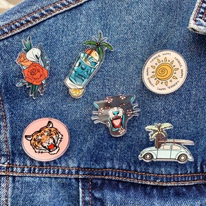 以下が含まれることがあります： 虎、豹、ドクロとクロスボーン、太陽、花、ビンテージカーの6つのカラフルなアイロン接着パッチのセット。パッチはすべて青いデニムの背景に配置されています。