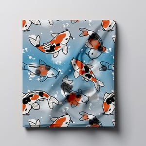 Könnte beinhalten: Ein Stofftextil mit einem sich wiederholenden Muster aus Koi-Fischen in den Farben Orange, Schwarz und Weiß. Die Fische sind vor einem hellblauen Hintergrund mit verstreuten weißen Farbspritzern und weichen, fließenden Falten abgebildet.