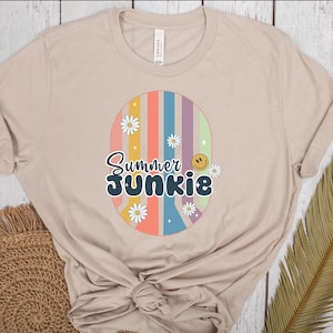 Könnte beinhalten: Ein beiges T-Shirt mit einem Peace-Zeichen-Motiv mit bunten Streifen und Gänseblümchen. Der Text "Summer Junkie" befindet sich im Peace-Zeichen.