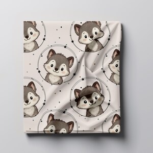 Könnte beinhalten: Gefalteter Stoff mit einem sich wiederholenden Muster von Cartoon-Wolfsgesichtern in kreisförmigen Rahmen. Die Wölfe haben graues Fell und rosige Wangen, vor einem cremefarbenen Hintergrund mit kleinen Sternen und Punkten. Geeignet für Kinderartikel.