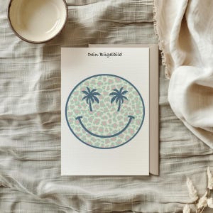 Könnte beinhalten: Eine weiße Karte mit dem Text "Dein Bügelbild" und einem blauen Smiley mit Palmen als Augen auf einem grün-rosa Leopardenmuster.