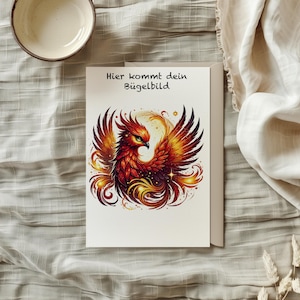 Könnte beinhalten: Eine weiße Karte mit dem Text "Hier kommt dein Bügelbild" und einer bunten Illustration eines Phönix mit roten, orangen und gelben Federn.