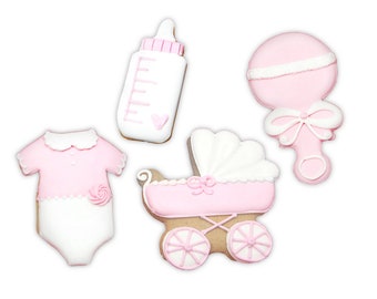 May include: A set of four baby-themed sugar cookies decorated with pink and white icing. The shapes include a baby bottle, a rattle with a bow, a onesie with a small rose detail, and a baby carriage with wheels and a scalloped hood design.