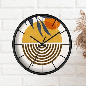 May include: A round clock with a black frame and white background. The clock face features a stylised design with a yellow sun, orange circle, and brown stripes. The clock hands are black.