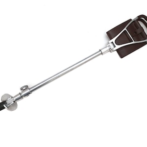 Puede incluir: Un bastón de paseo de color plateado con un mango de cuero marrón. El mango tiene un lazo en la parte superior y una correa en el lateral.