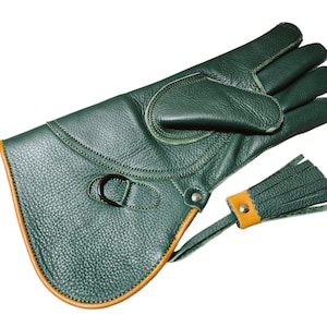 May include: A dark green leather falconry glove with a textured surface. The glove has a contrasting tan trim and a buckle closure. A small leather tassel is attached to the wrist area.