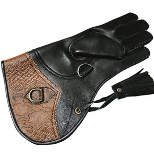 Può includere: Guanti in pelle nera con un motivo a pelle di serpente marrone sul dorso della mano. I guanti hanno un cinturino con una fibbia e un fiocco.
