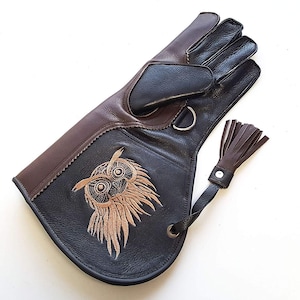 以下が含まれることがあります： 刺繍されたフクロウのデザインが施された、茶色と黒の革手袋。手袋にはタッセルと指ループが付いています。