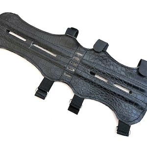 May include: Black leather archery arm guard with adjustable straps and a crocodile-embossed design.