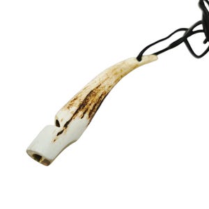 May include: A white antler whistle with a brown pattern, attached to a black cord. The whistle is about 5 inches long.