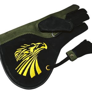 Puede incluir: Un guante de tiro con arco de cuero verde y negro con un diseño de águila bordado en amarillo en la parte posterior. El guante tiene un borla en la muñeca.