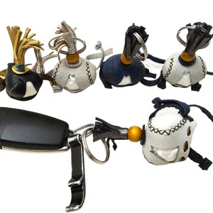 Puede incluir: Un conjunto de cinco llaveros de cuero con bolas de cuero de diferentes colores y detalles dorados. Cada llavero tiene un pequeño borla y un anillo para sujetar las llaves.