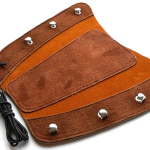 Könnte beinhalten: Braunes Leder-Bogenschießen-Armguard mit Wildlederfutter und Metallschnallen. Das Armguard ist so konzipiert, dass es den Arm vor der Sehne eines Bogens schützt.