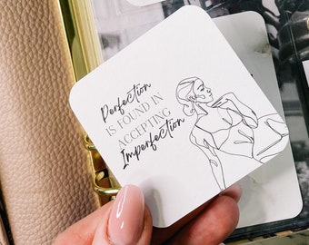 May include: White card with black text and a line drawing of a woman. The text reads "Perfection is found in accepting imperfection."