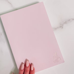 May include: A light pink notebook with a silver rose design on the front cover.