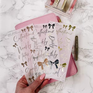 Peut inclure: Quatre feuilles d'autocollants de planificateur en feuille d'or avec des nœuds et du texte manuscrit. Le texte comprend "Collections", "Hebdomadaire", "Notes", "Objectifs", "Quotidien", "Mensuel", "À faire" et "Journal".