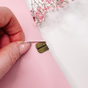 Könnte beinhalten: Ein rosa Notizbuch mit einem messingfarbenen Verschluss und einem elastischen Verschluss. Das Notizbuch ist teilweise geöffnet und zeigt die Innenseiten. Rosa Blüten befinden sich im Hintergrund.