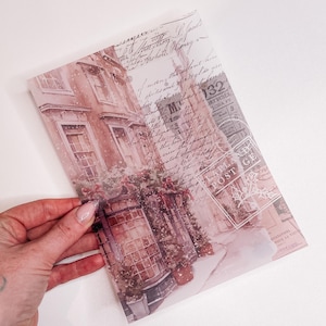 May include: A vintage-style translucent sheet with a watercolor illustration of a snowy street scene with a building and a garland. The sheet has a faded, antique look with handwritten text and a postage stamp.