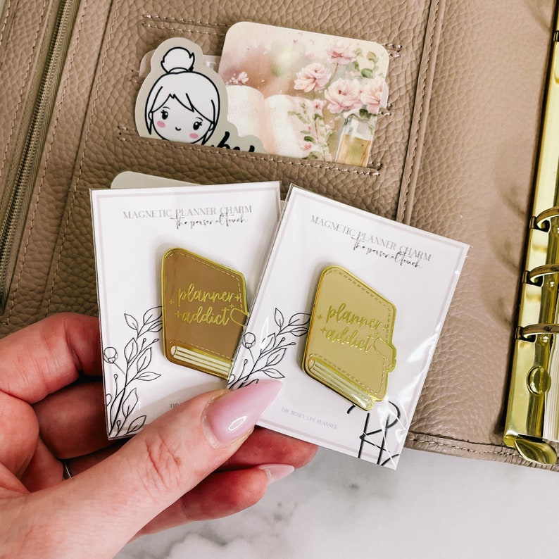 May include: Two gold planner charms with a book design and the text "planner addict" on a white background. The charms are magnetic and are designed to be used in a planner.