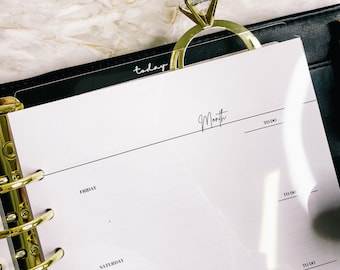 Könnte beinhalten: Ein weißer Planer mit einem goldenen Ringbuch. Der Planer hat eine schwarze Lasche mit der Aufschrift "heute" und einen Abschnitt mit der Bezeichnung "Monat" mit einer "To Do"-Liste. Der Planer ist auf einer Seite mit den Tagen Freitag und Samstag geöffnet.