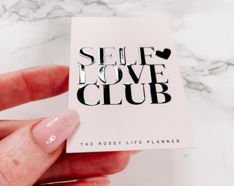 May include: A pink card with silver foil lettering that reads "SELF LOVE CLUB" and "THE ROSEY LIFE PLANNER".