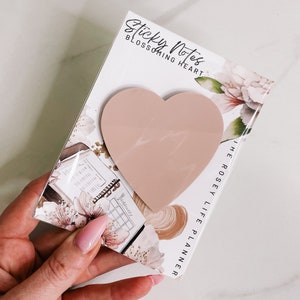May include: A pack of pink heart-shaped sticky notes with the text "Sticky Notes Blossoming Heart The Rosely Life Planner" on the front.