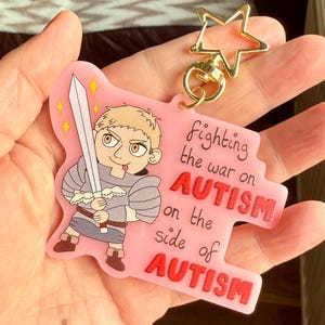 May include: Pink keychain featuring a cartoon knight with a sword. The text on the keychain reads "fighting the war on AUTISM on the side of AUTISM". It has a gold star-shaped clasp.