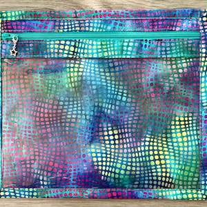 May include: A rectangular, handmade fabric pouch with a vibrant, multicolored spotted pattern in shades of blue, green, pink, and yellow. It features a turquoise zipper and a small star-shaped charm. The pouch is designed for storage.