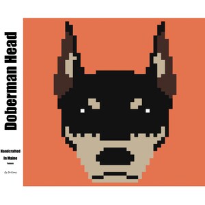 May include: Pixelated Doberman head illustration on an orange background. The dog's head is black, tan, and brown. The text "Doberman Head" is vertically aligned on the left side. The text "Handcrafted in Maine" and "Pattern by Brittany" are also included.