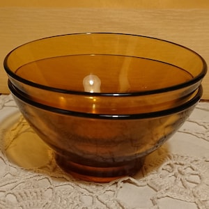 Peut inclure: Deux bols en verre ambré empilés l'un sur l'autre. Les bols sont sur une nappe en crochet blanche.