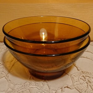 Peut inclure: Deux bols en verre ambré empilés l'un sur l'autre. Les bols sont ronds et ont une légère lèvre autour du bord supérieur.