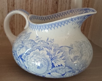 May include: A white ceramic pitcher with a blue floral design. The pitcher has a rounded body and a handle.