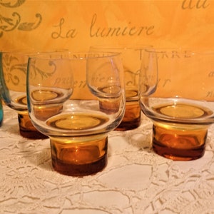 May include: Set of four amber-colored glass tumblers with a clear glass top. The glasses have a wide base and a rounded bowl.