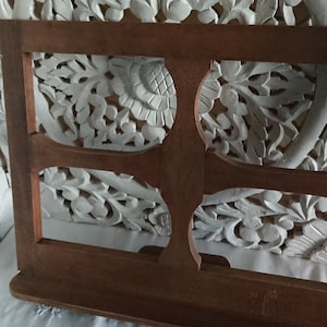 May include: A wooden book stand with four open rectangular spaces. The stand is made of dark brown wood and has a simple design. The stand is in front of a white carved wooden background.