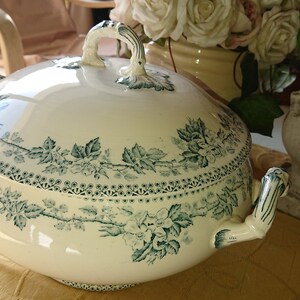 Peut inclure: Un plat de service en porcelaine blanche avec un motif floral vert. Le plat a un couvercle avec une poignée décorative.