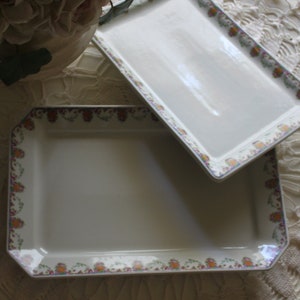 May include: Two white ceramic serving trays with floral patterns. The top tray is rectangular and the bottom tray is square with rounded corners.