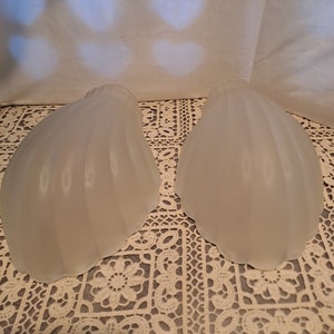 May include: Two white frosted glass lampshades with a scalloped design. The lampshades are sitting on a white lace tablecloth.