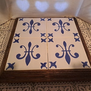 Può includere: Un sottopentola in piastrelle di legno con un motivo floreale blu e bianco. Il sottopentola è composto da quattro piastrelle quadrate con una cornice in legno.