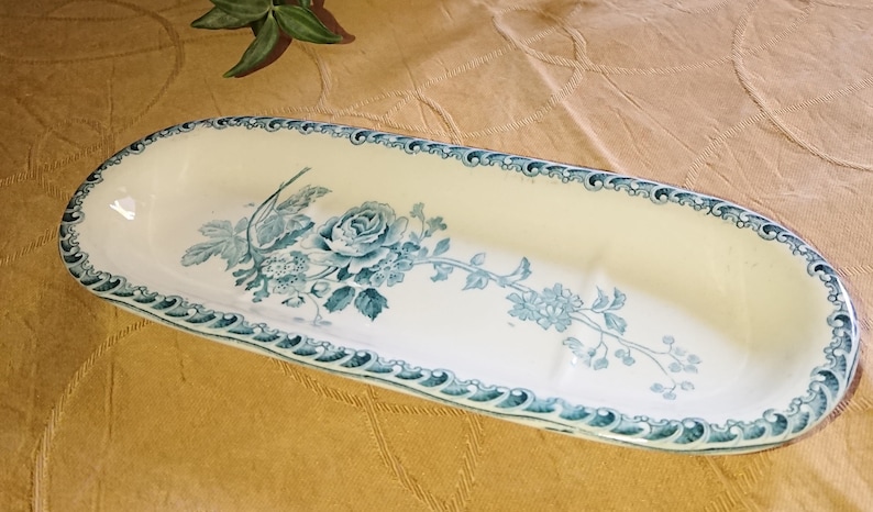 May include: A white oval ceramic dish with a blue floral design. The dish has a raised edge and a scalloped rim.