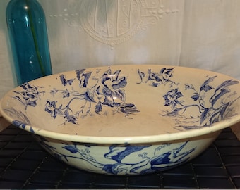 May include: A large, white ceramic bowl with a blue floral pattern. The bowl is decorated with blue flowers and leaves on a white background.