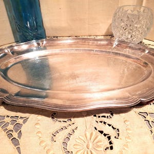 Puede incluir: Una bandeja de servir ovalada de plata con un borde decorativo festoneado.