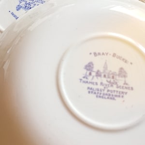 Op de afbeelding: Een witte keramische schotel met een blauw en wit ontwerp. De schotel heeft de tekst "Bray-Bucks" en "Thames River Scenes" gedrukt op de onderkant. De tekst bevat ook "Palisy Pottery Staffordshire England".