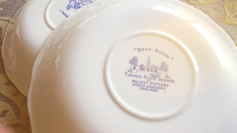 Op de afbeelding: Een witte keramische schotel met een blauw en wit ontwerp. De schotel heeft de tekst "Bray-Bucks" en "Thames River Scenes" gedrukt op de onderkant. De tekst bevat ook "Palisy Pottery Staffordshire England".