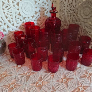 May include: A set of 15 red glass tumblers and a matching decanter with a stopper. The glasses and decanter have a textured, embossed design.